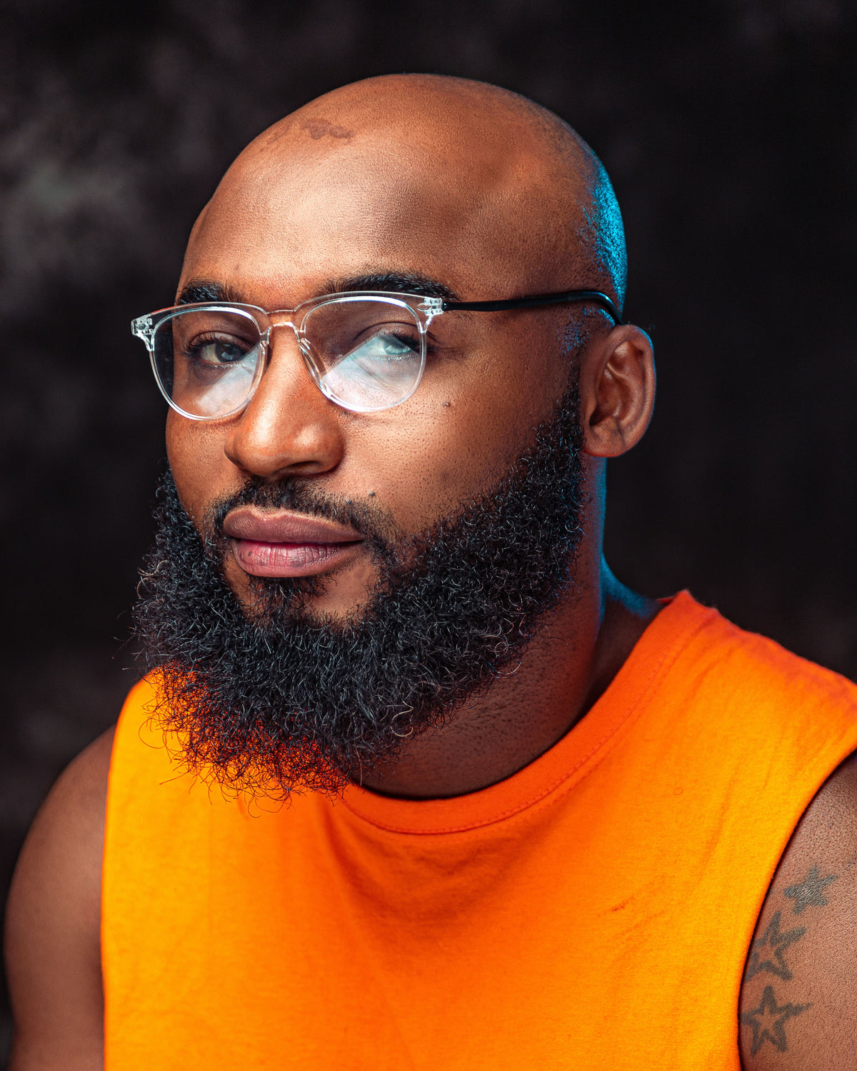 Man wearing glasses and a plain orange sleeveless top