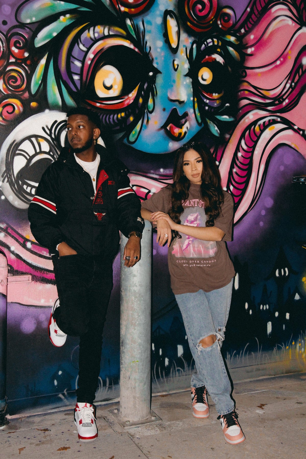 Man and woman in casual streetwear standing together against colourful graffiti